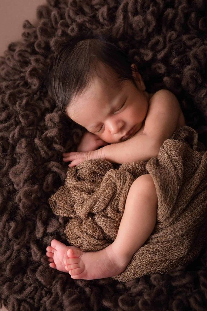 baby photography Sydney newborn is curled up on a brown cushion