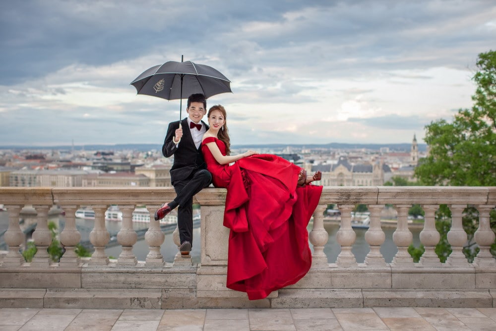 wedding photography in singapore the groom and bride are sitting on the edge of the building and the groom is holding an umbrella