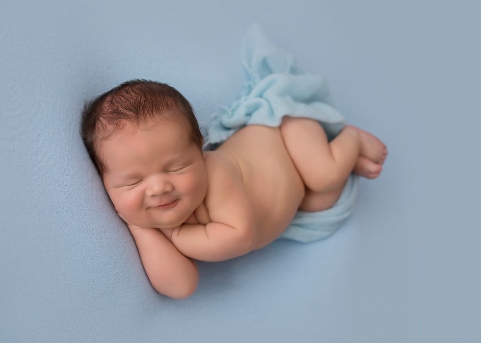 Sydney newborn photography baby is sleeping and smiling on a blue bed