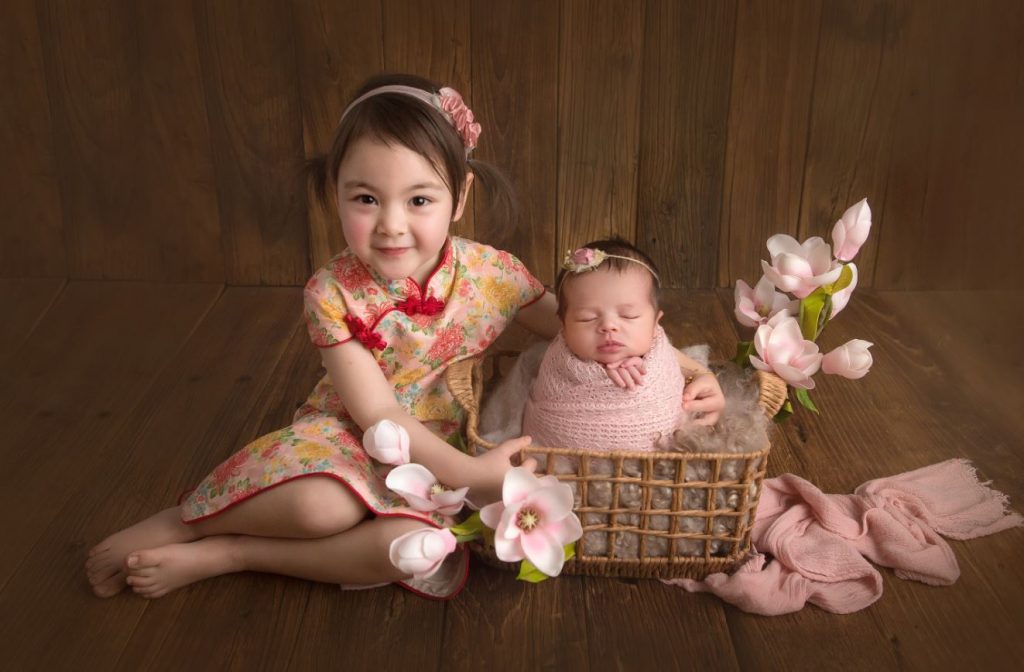 newborn photography Sydney sister in a traditional chinese outfit is posing next to her new younger sister