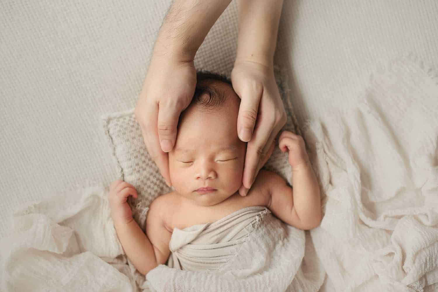newborn photography singapore baby sleeping peacefully with the fathers gently holding the head