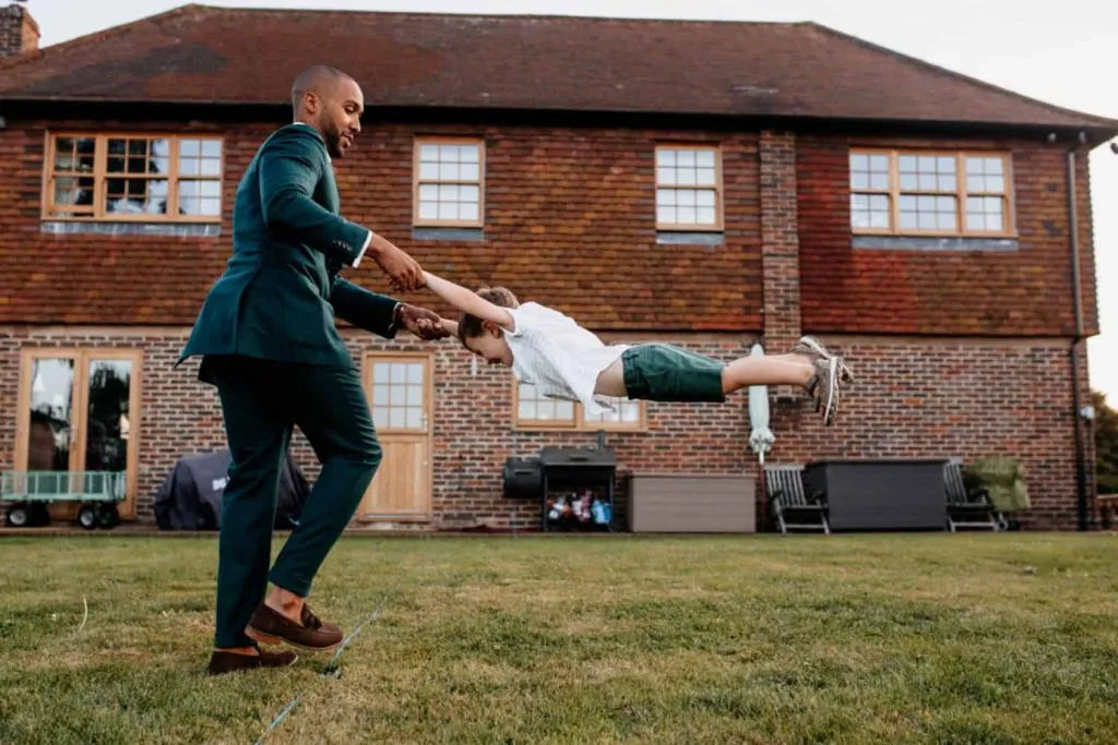 London wedding photographer groom is lifting up the kid in the green shorts