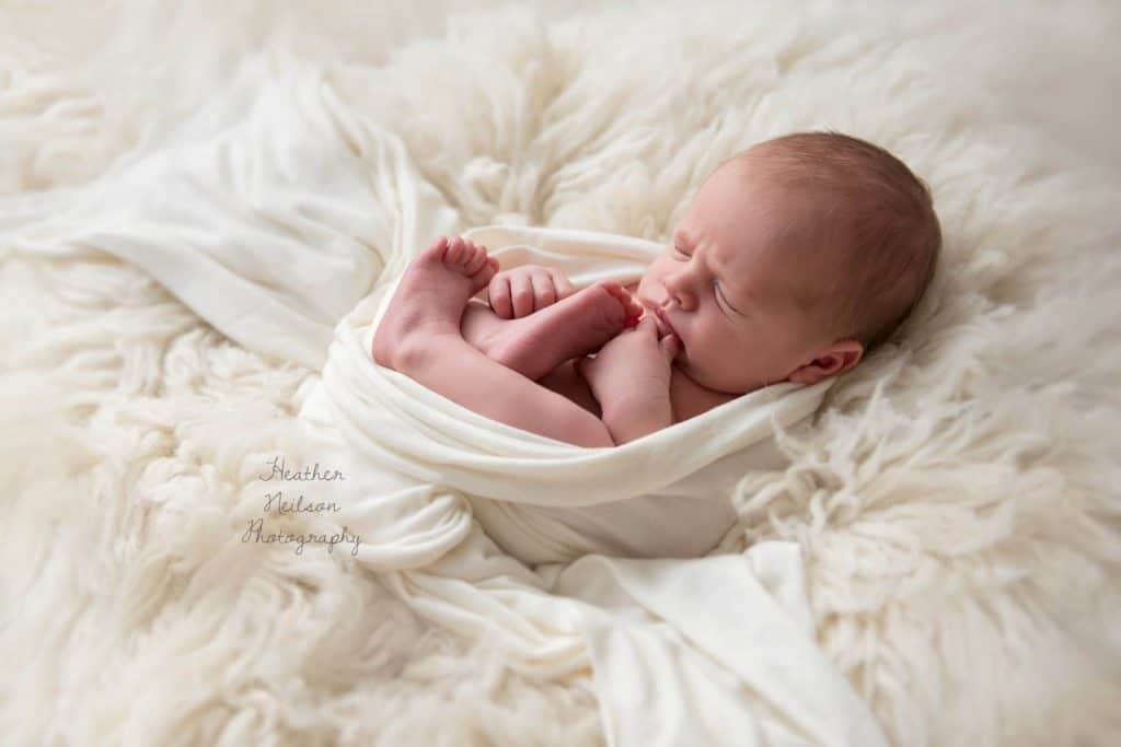 baby photoshoot London newborn is curled up and sleeping on fluffy bed and blanket