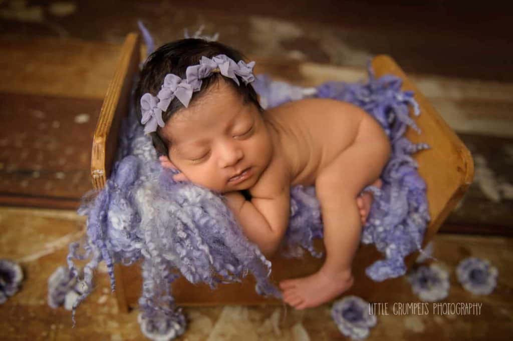 baby photographer Londonnewborn with a purple headband is sleeping on purple flowers