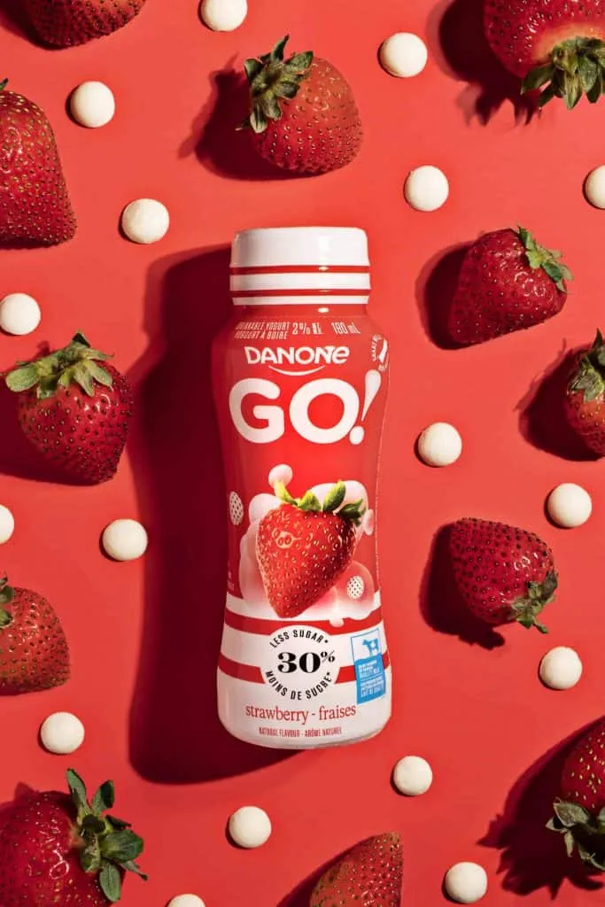 A bottle of danco go surrounded by strawberries on a red background, perfect for food photographers in Toronto.