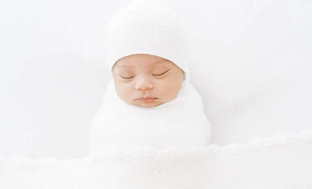 A newborn baby peacefully sleeping in a white blanket, captured by talented newborn photographers in Toronto.