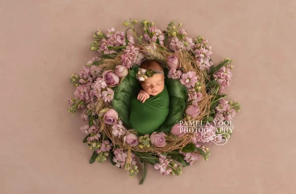 A newborn baby is wrapped in a green blanket surrounded by a wreath of flowers, captured beautifully by newborn photographers in Toronto.